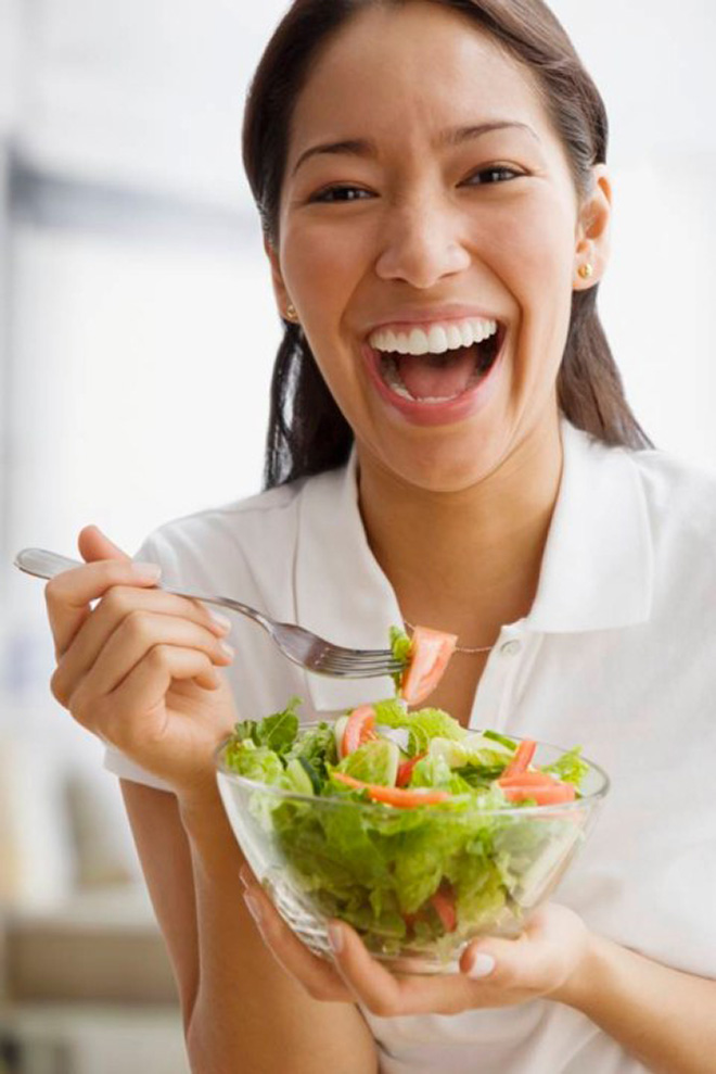 Woman laughing alone with salad.